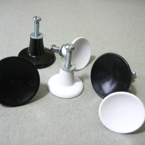 May include: Six cabinet knobs, three black and three white, with a screw-on design. The knobs have a rounded, slightly domed shape.