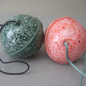 May include: Two round, speckled ornaments with cords. One ornament is green with white speckles and the other is red with white speckles.