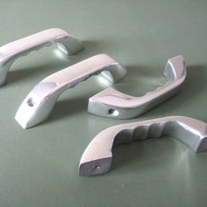 May include: Four silver-coloured metal handles with different designs. Two handles have a smooth surface, one has a textured surface, and one has a ribbed surface.