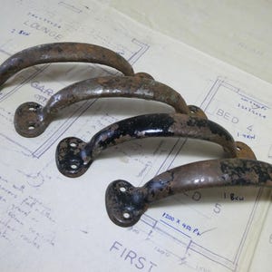 May include: Four antique, weathered metal door handles with a curved design. The handles are various shades of brown and black, showing signs of age and wear. They are set against a vintage blueprint background.