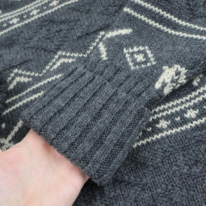 May include: Gray knitted sweater with a white geometric pattern. The sweater has a ribbed cuff.