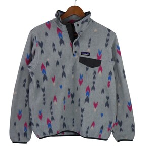 Può includere: Un pullover in pile grigio con un motivo a frecce rosa, blu e navy. Il pullover ha un colletto, una tasca e una paramontura con bottoni neri. Il logo Patagonia è sulla tasca.