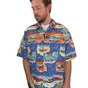 Puede incluir: Una camisa azul de manga corta con botones y un estampado colorido de coches antiguos y paisajes.