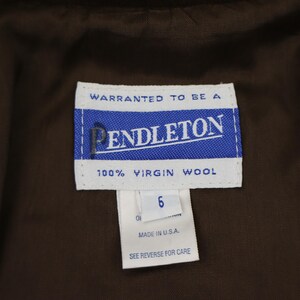 K&ouml;nnte beinhalten: Nahaufnahme eines Pendleton-Etiketts mit dem Markennamen in Wei&szlig; auf blauem Hintergrund. Das Etikett enth&auml;lt auch die Aufschrift "100% Virgin Wool" und "Made in U.S.A.". Das Gr&ouml;&szlig;enetikett zeigt "6".