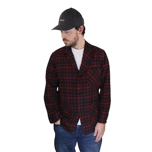 May include: A red and black plaid flannel shirt jacket with a button closure and a single pocket on the left chest. The jacket is worn over a white t-shirt and blue jeans.