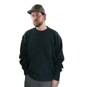 Pu&ograve; includere: Un maglione girocollo verde scuro e un berretto da baseball verde con una piccola toppa rettangolare. Il maglione ha un aspetto strutturato. Il berretto ha una visiera piatta.
