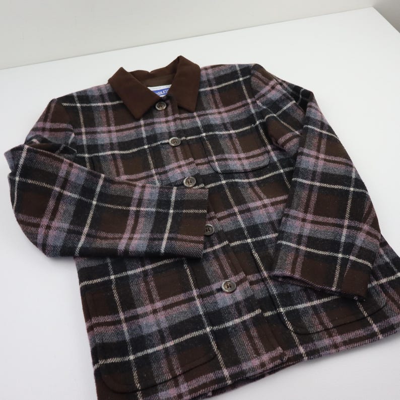 K&ouml;nnte beinhalten: Eine braune, schwarze und graue karierte Jacke mit braunem Kragen und Knopfverschluss. Die Jacke hat ein klassisches Design mit taillierter Passform. Der Stoff scheint eine Wollmischung zu sein. Die Jacke hat zwei Vordertaschen.