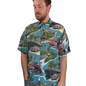 以下が含まれることがあります： ヴィンテージカーとヤシの木がプリントされた、ターコイズブルーの半袖シャツ。シャツには、赤いオープンカー、青いセダン、黒いステーションワゴンなど、さまざまな車が描かれています。プリントには、ヤシの木、ビーチの風景、そして「ハリウッド」という言葉も含まれています。