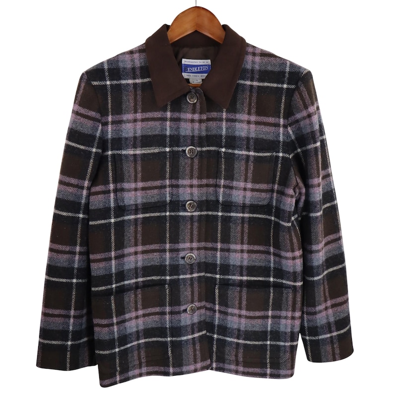 K&ouml;nnte beinhalten: Eine braun, lila und wei&szlig; karierte Jacke mit braunem Kragen und Kn&ouml;pfen. Die Jacke h&auml;ngt an einem Holzb&uuml;gel. Der Markenname "Pendleton" ist auf dem Kragen sichtbar.