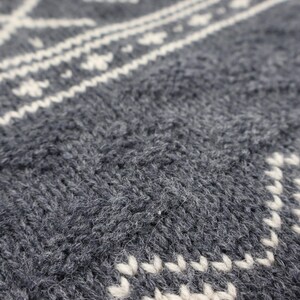 May include: Close-up of a gray knitted fabric with a white patterned design. The fabric is soft and textured, with a fuzzy appearance.