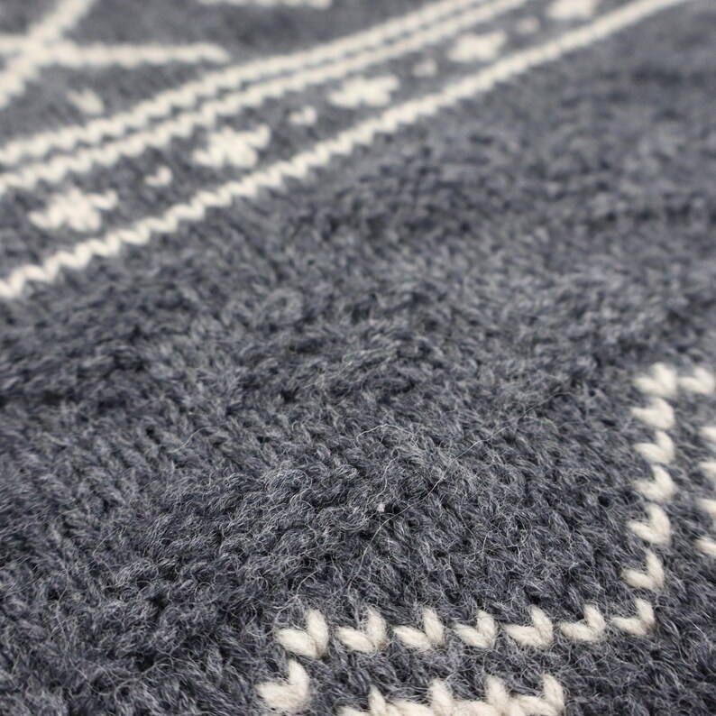 May include: Close-up of a gray knitted fabric with a white patterned design. The fabric is soft and textured, with a fuzzy appearance.