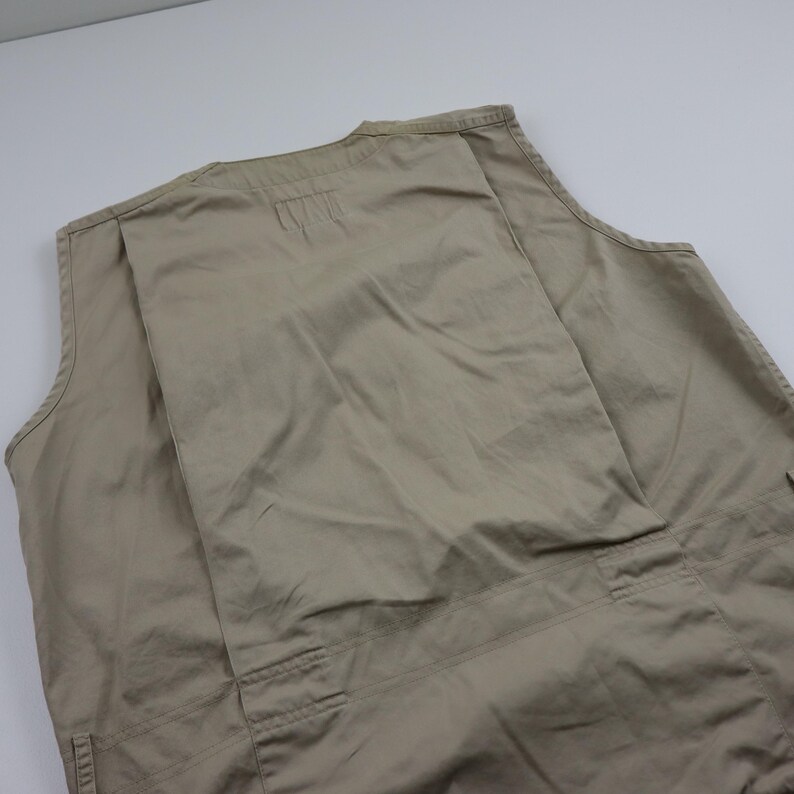 May include: A beige sleeveless vest with multiple pockets. The vest is made of a lightweight fabric and has a relaxed fit.