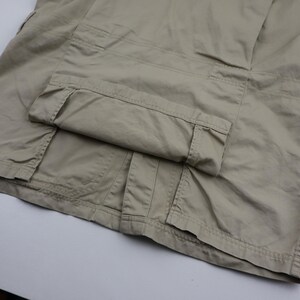 May include: A pair of beige cargo pants with a folded cuff. The pants have multiple pockets and a belt loop.