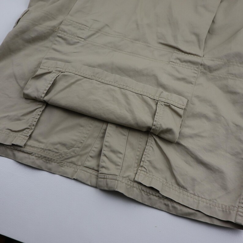 May include: A pair of beige cargo pants with a folded cuff. The pants have multiple pockets and a belt loop.