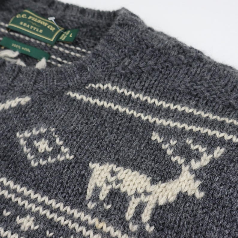 May include: A gray knitted sweater with a white reindeer pattern. The sweater has a crew neck and is made of a soft, warm material. The label on the sweater reads "G.C.  Pearson Co. Seattle."
