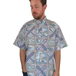 Puede incluir: Una camisa de manga corta con botones y un estampado hawaiano colorido con palmeras, flores y un surfista. La camisa es azul claro con detalles en rosa, verde y marrón.
