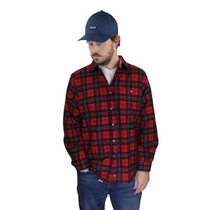 以下が含まれることがあります： ボタンダウンのフロントと長袖の赤と黒の格子縞のフランネルシャツ。シャツは青い野球帽をかぶった人が着用しています。
