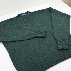 Pu&ograve; includere: Un maglione verde scuro a girocollo con polsini e orlo a coste. Il maglione ha un'etichetta sul retro del collo. Il maglione &egrave; realizzato in un materiale morbido e strutturato.