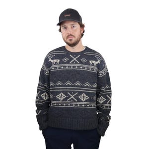 May include: A dark gray sweater with a white and gray fair isle pattern featuring reindeer and geometric designs. The sweater has a crew neck and long sleeves.