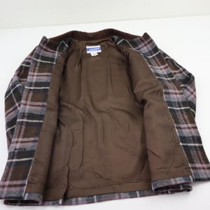 K&ouml;nnte beinhalten: Eine karierte Jacke in Braun-, Grau- und Lavendelt&ouml;nen mit braunem Innenfutter. Die Jacke ist offen und zeigt das Futter und ein kleines Etikett. Das Design ist klassisch und ma&szlig;geschneidert, ideal f&uuml;r k&uuml;hleres Wetter.