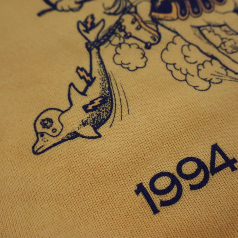 Puede incluir: Sudadera amarilla con un gr&aacute;fico de delf&iacute;n azul y el a&ntilde;o 1994 impreso en la parte inferior.