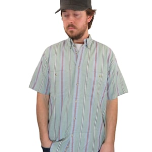 May include: A light blue and green striped short-sleeved button-down shirt with a black baseball cap.
