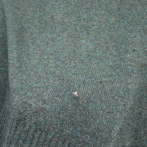 Pu&ograve; includere: Primo piano di un tessuto a maglia color verde acqua. Il tessuto ha un aspetto strutturato con linee di maglia visibili e una piccola macchia di colore chiaro. La trama generale suggerisce un maglione o un capo simile.