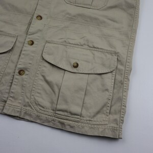 May include: A beige utility jacket with a button closure and multiple pockets. The jacket has a flap pocket on the chest and two large pockets on the front.