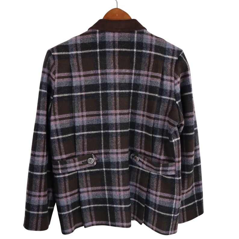 K&ouml;nnte beinhalten: Ein brauner, schwarzer und lavendelfarbener Blazer mit Karomuster, einem braunen Kragen und zwei Vordertaschen. Der Blazer h&auml;ngt an einem Holzb&uuml;gel.