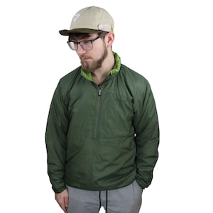 以下が含まれることがあります： 緑色の軽量ジッパー付きジャケットで、半分までジッパーで閉じられます。ジャケットは緑とベージュのカラーリングで、撥水素材で作られています。