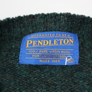 Pu&ograve; includere: Primo piano di un maglione lavorato a maglia verde scuro con un'etichetta blu. L'etichetta recita "PENDLETON" e "100% PURE VIRGIN WOOL, PORTLAND OREGON, SINCE 1863". Il maglione &egrave; XL.