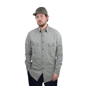 Puede incluir: Una camisa de manga larga de color verde claro con botones y dos bolsillos en el pecho. La camisa está hecha de una tela suave y cómoda y tiene un corte holgado. El modelo lleva una gorra de béisbol verde con un pequeño logotipo en la parte delantera.