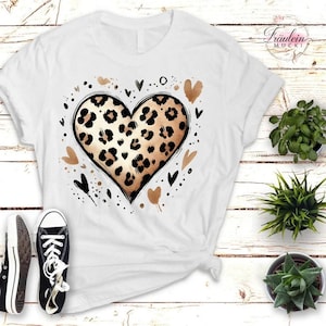 Könnte beinhalten: Weißes T-Shirt mit einem Leopardenmuster-Herz-Design. Das Herz ist schwarz umrandet und von kleinen schwarzen und goldenen Herzen und Punkten umgeben. Das Shirt wird mit schwarzen Turnschuhen kombiniert.