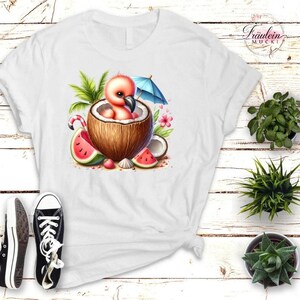 Könnte beinhalten: Weißes T-Shirt mit einer skurrilen Illustration eines Flamingo-Küken in einer Kokosnussschale, komplett mit blauem Sonnenschirm, Wassermelonenscheiben und tropischem Laub. Das Design ist lebendig und farbenfroh.