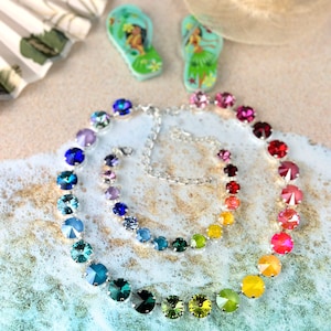 May include: A rainbow crystal necklace with a silver chain and a matching bracelet. The necklace and bracelet are made of round, faceted crystals in a rainbow of colours, including blue, green, yellow, orange, red, and pink.