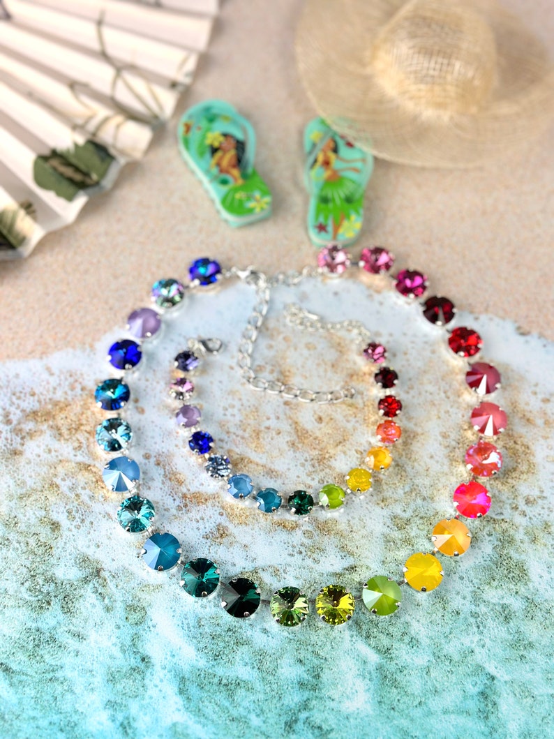 May include: A rainbow crystal necklace with a silver chain and a matching bracelet. The necklace and bracelet are made of round, faceted crystals in a rainbow of colours, including blue, green, yellow, orange, red, and pink.
