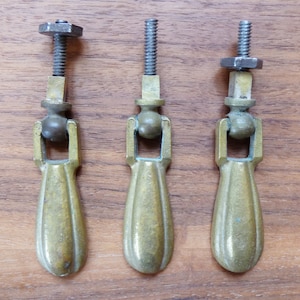 Pode incluir: Três botões de armário de latão com forma de lágrima e uma bola redonda no topo. Cada botão tem um parafuso roscado para fixar a uma porta de armário.