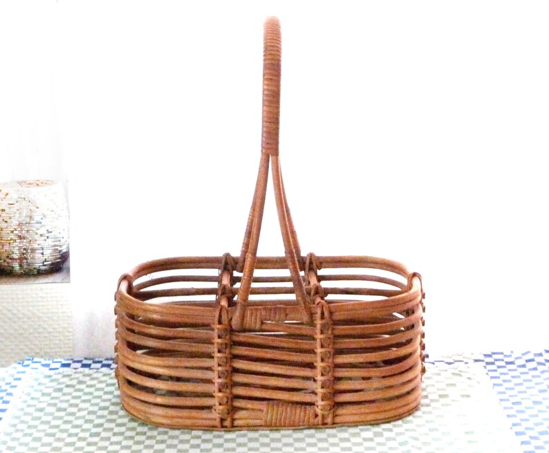 May include: A brown wicker basket with a single handle. The basket has a rectangular shape with a rounded bottom and is designed to hold bottles.