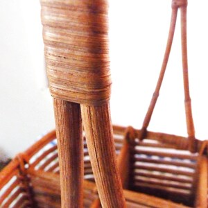 May include: Close-up of the woven handle of a brown wicker basket. The handle is made of two pieces of woven wicker that are joined together at the top.
