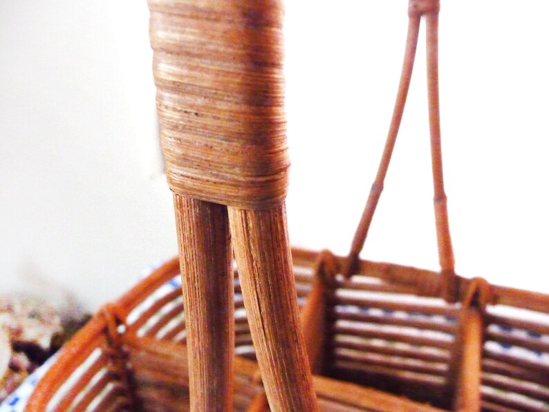 May include: Close-up of the woven handle of a brown wicker basket. The handle is made of two pieces of woven wicker that are joined together at the top.