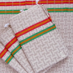 May include: Beige linen kitchen towels with a geometric pattern and colorful stripes in red, orange, and green. The towels are folded and stacked, with a tag attached to one. The towels are made of a woven fabric.