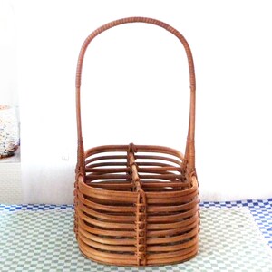 May include: A brown wicker bottle carrier with a handle. The carrier has four compartments for bottles.