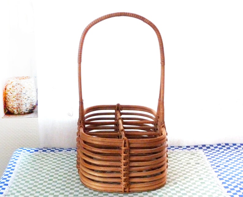 May include: A brown wicker bottle carrier with a handle. The carrier has four compartments for bottles.