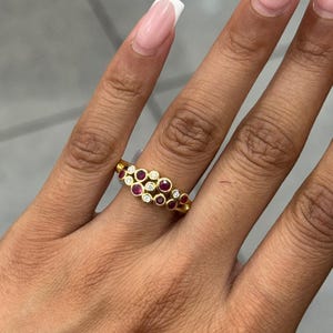 Peut inclure: Une bague en or ornée d'un groupe de rubis rouges et de diamants blancs transparents de taille ronde, sertis dans des chatons individuels. Les pierres sont disposées en un motif décalé et multicouche sur l'anneau, créant un design texturé.