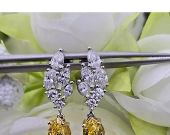 May include: A pair of elegant earrings featuring a cluster of clear, sparkling stones and a large, yellow pear-shaped gemstone. The earrings are set in a silver metal with a gold-colored setting for the yellow stone.