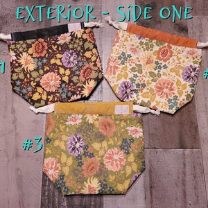 May include: Three floral drawstring bags in a variety of colors. The bags feature a mix of floral patterns with colors including brown, orange, purple, and green. The bags are labeled with the text "Exterior - Side One".