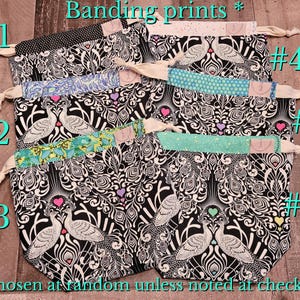 May include: Six drawstring bags with various patterned bands. The bags feature a black and white peacock feather design. The bands are in different colors and patterns, including polka dots, floral, and geometric shapes. The text "Banding prints" and numbers are visible.