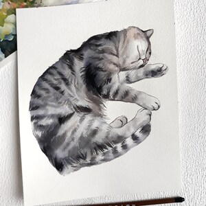 May include: Watercolour painting of a grey tabby cat sleeping on its side. The cat is curled up with its head resting on its paws.