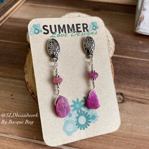 Puede incluir: Un par de pendientes colgantes con gotas de piedras preciosas rosas y abalorios de filigrana plateada. Los pendientes se muestran en una tarjeta con el texto "Summer Love Designs" y "@SLDbeadwork By Basque Bug".