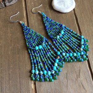 May include: A pair of long, beaded earrings with a turquoise and blue color scheme. The earrings are made with small, glass beads and feature a cascading design.